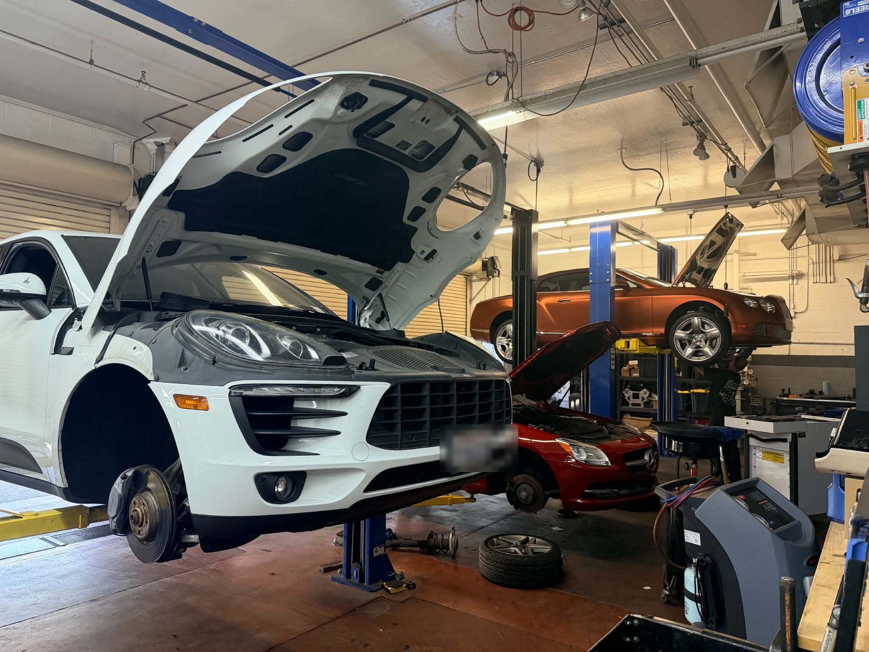 Vehicles on lifts inside the Dream Garage AZ service bays in Scottsdale, including a Porsche SUV and a Bentley coupe.